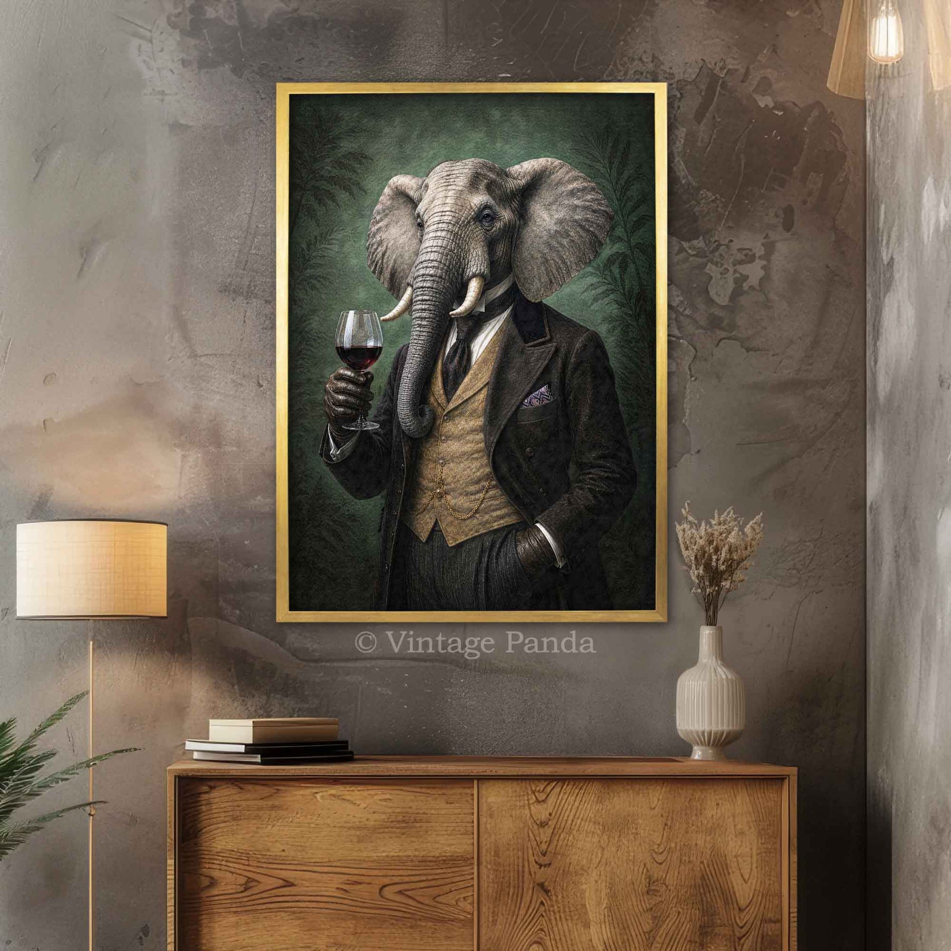 A framed vertical art print depicting a Victorian-style elephant in a black suit holding a glass of red wine, displayed on a textured gray wall above a wooden console table in a styled room in a gold frame.