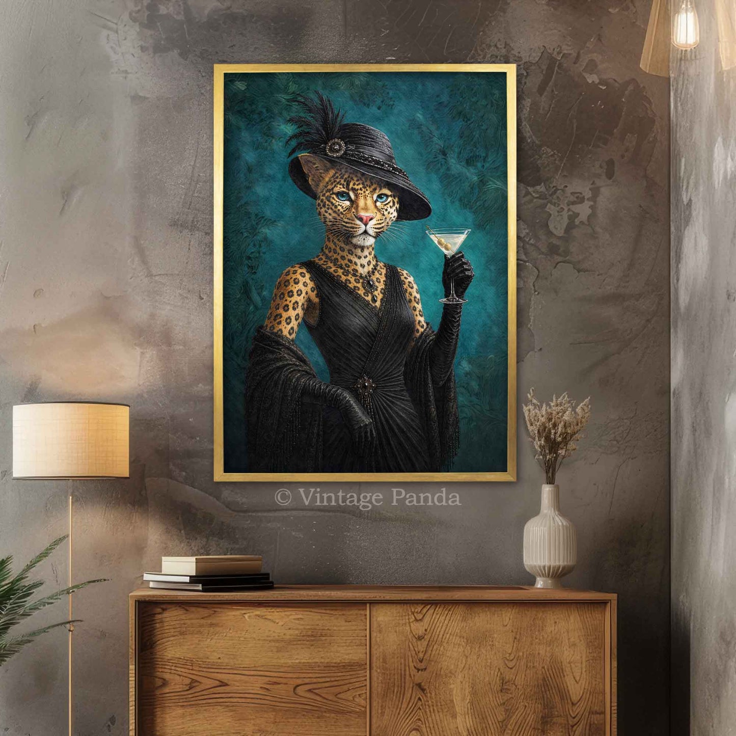A framed vertical art print depicting a leopard dressed in a black hat and dress while holding a martini glass, displayed on a textured gray wall above a wooden console table with lamps and a vase.