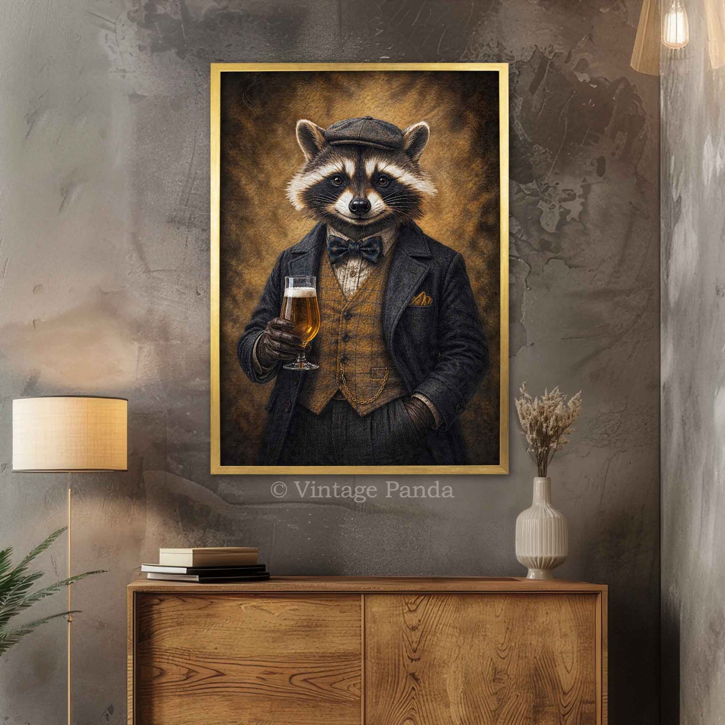 A framed vertical portrait print of a raccoon dressed in a dark suit and bow tie, holding a glass of beer, displayed on a gray textured wall above a wooden cabinet in a styled interior.