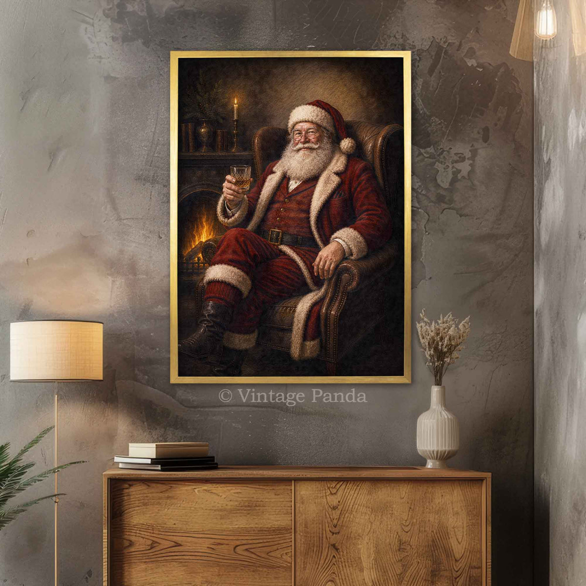 A framed vertical canvas print of a classic Christmas painting featuring Santa Claus in his red suit sitting by a fireplace with a glass of whisky, hanging on a textured gray wall above a wooden cabinet in a styled room.