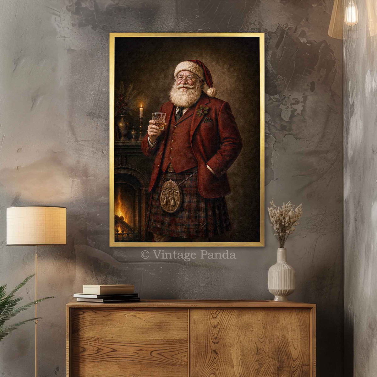 A framed vertical art print depicting a jovial Scottish Santa Claus in a red coat and kilt holding a glass of whiskey, styled on a textured gray wall above a wooden console table with a lamp and vase.