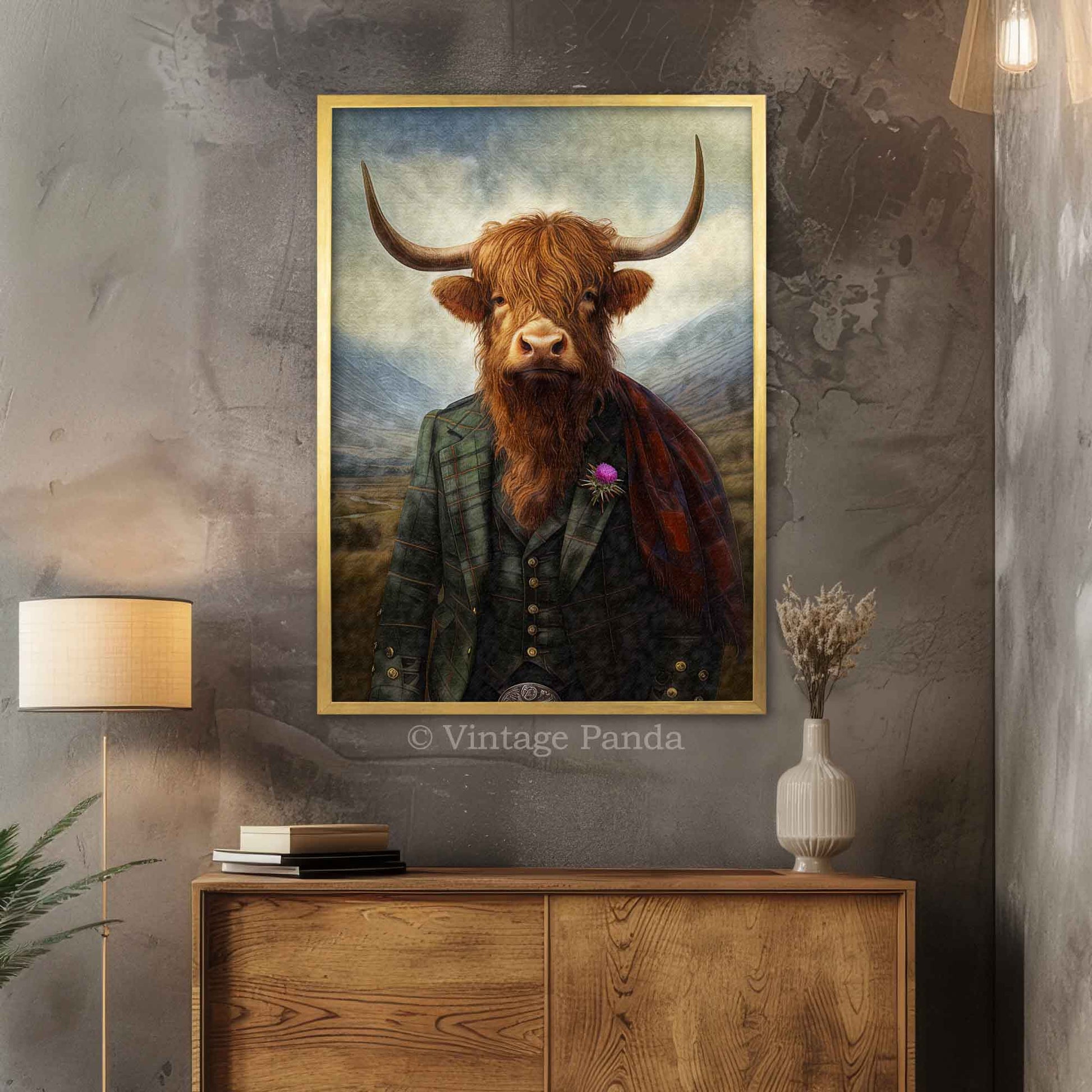 Framed artwork of a Highland cow with a traditional Scottish kilt outfit on a wall above a wooden cabinet in a gold frame.