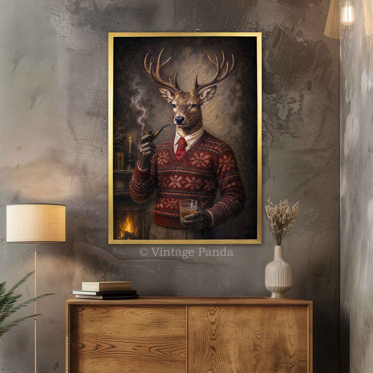 A framed vertical art print featuring a deer dressed in a red patterned holiday sweater and holding a pipe and glass of whisky, displayed on a textured gray wall above a wooden cabinet in a styled room.
